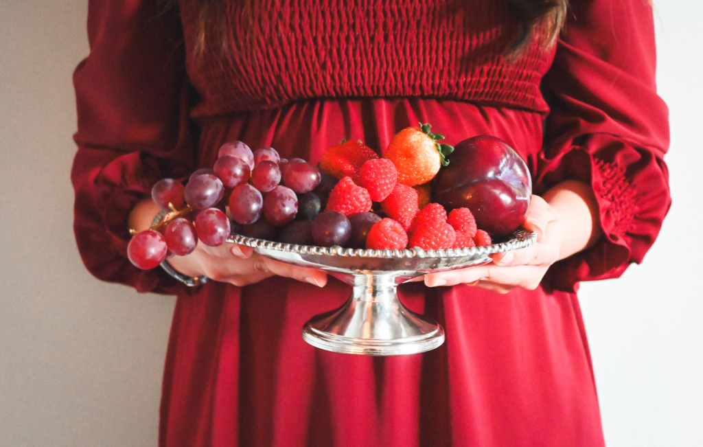 Silver compotier with fruit held by woman in red dress