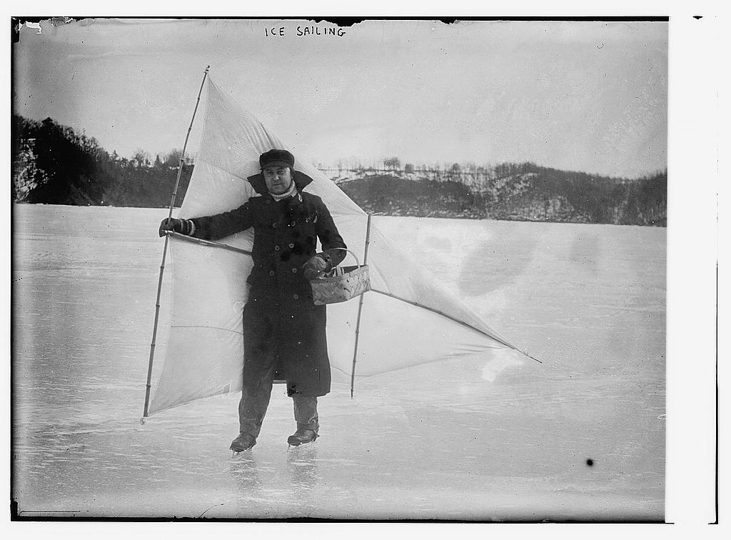 Black and white historical photograph of man holding a sail on the ice for ice sailing.