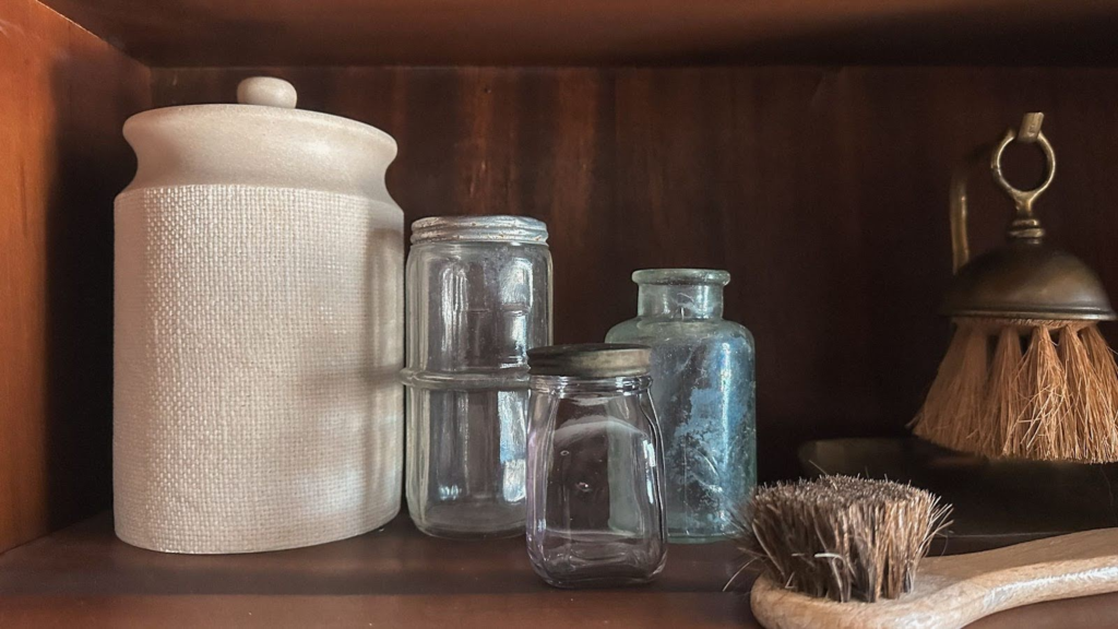 Multiple sized vases and glasses on a dark wood background with a bristle brush in the front