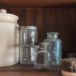 Sea glass jars and white jar sitting in front of dark wood background with bristle brush