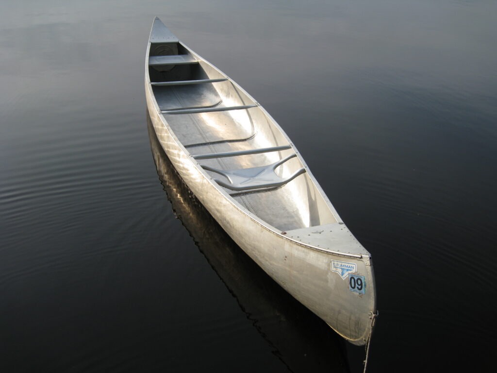 A silver canoe floating on the calm, mirror-like water of a lake in the Boundary Waters Canoe Area Wilderness