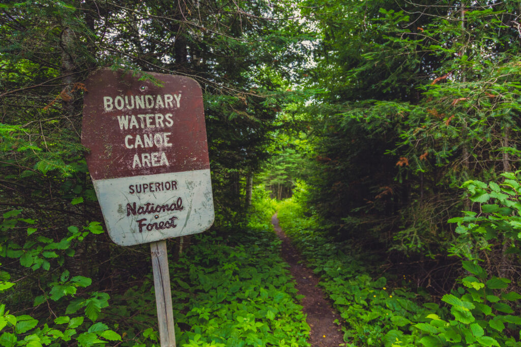 A wooden Boundary Waters Canoe Area Wilderness sign at the start of a forested portage trail in Minnesota.