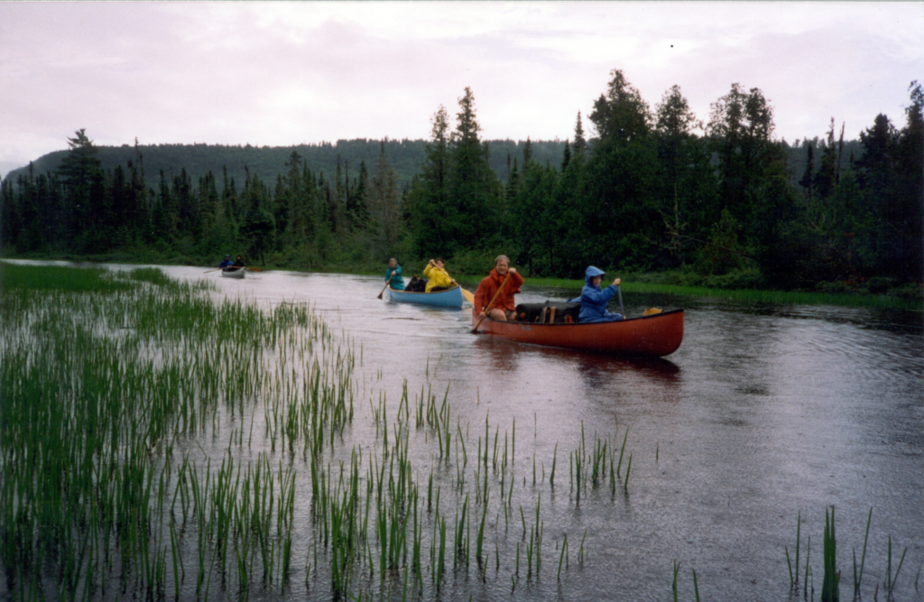 A person in a red canoe paddling down the wide Rainy River on the border of the Boundary Waters Canoe Area Wilderness.