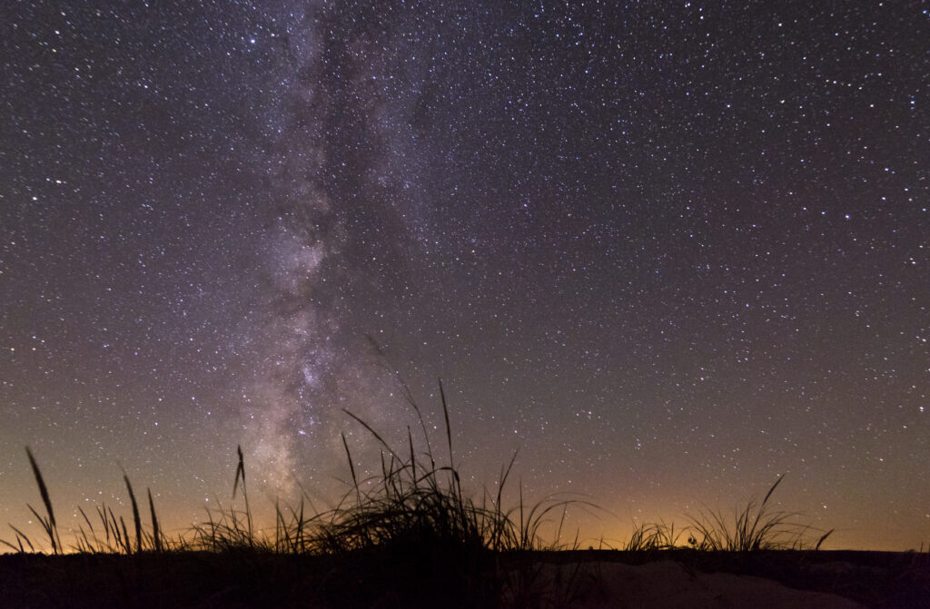 The Milky Way galaxy shining brightly over the silhouetted dune trail.