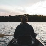 Rear view of a person paddling a canoe on a calm lake in the Boundary Waters at sunset.