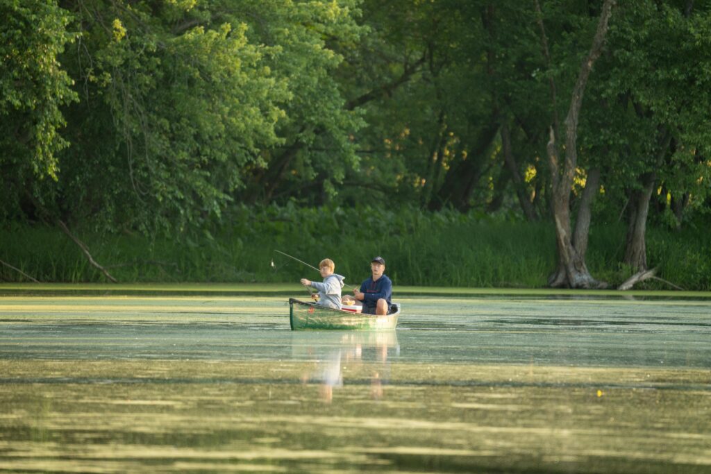 Two people fishing from a green canoe in the Boundary Waters Canoe Area.