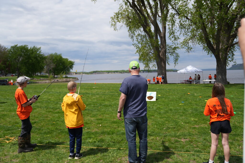 Governor Tim Walz demonstrating to three kids how to cast a reel.