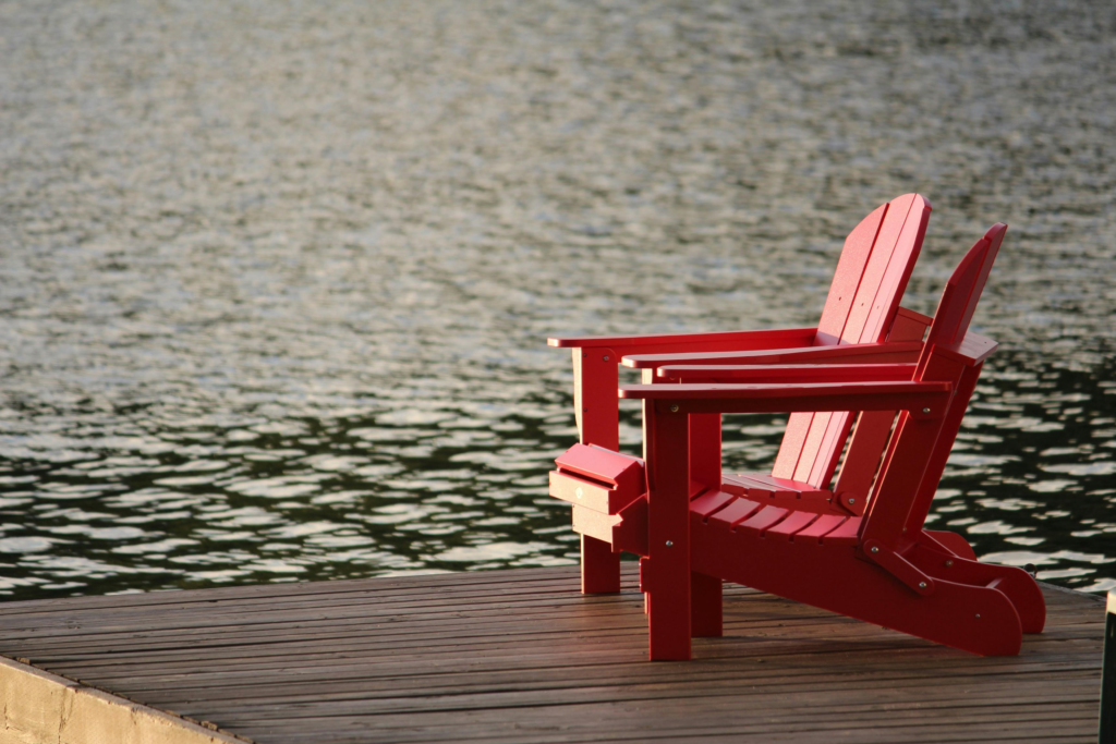 Two red Adirondack chairs sitting on docks on water.