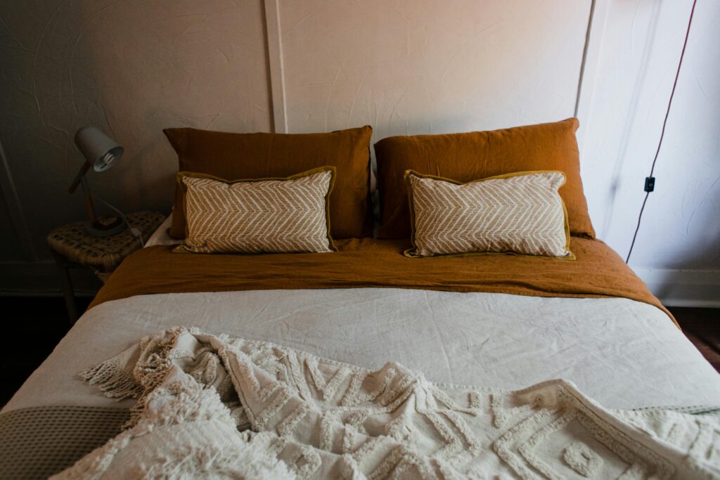 Bed with white comforter and ochre sheets and pillows