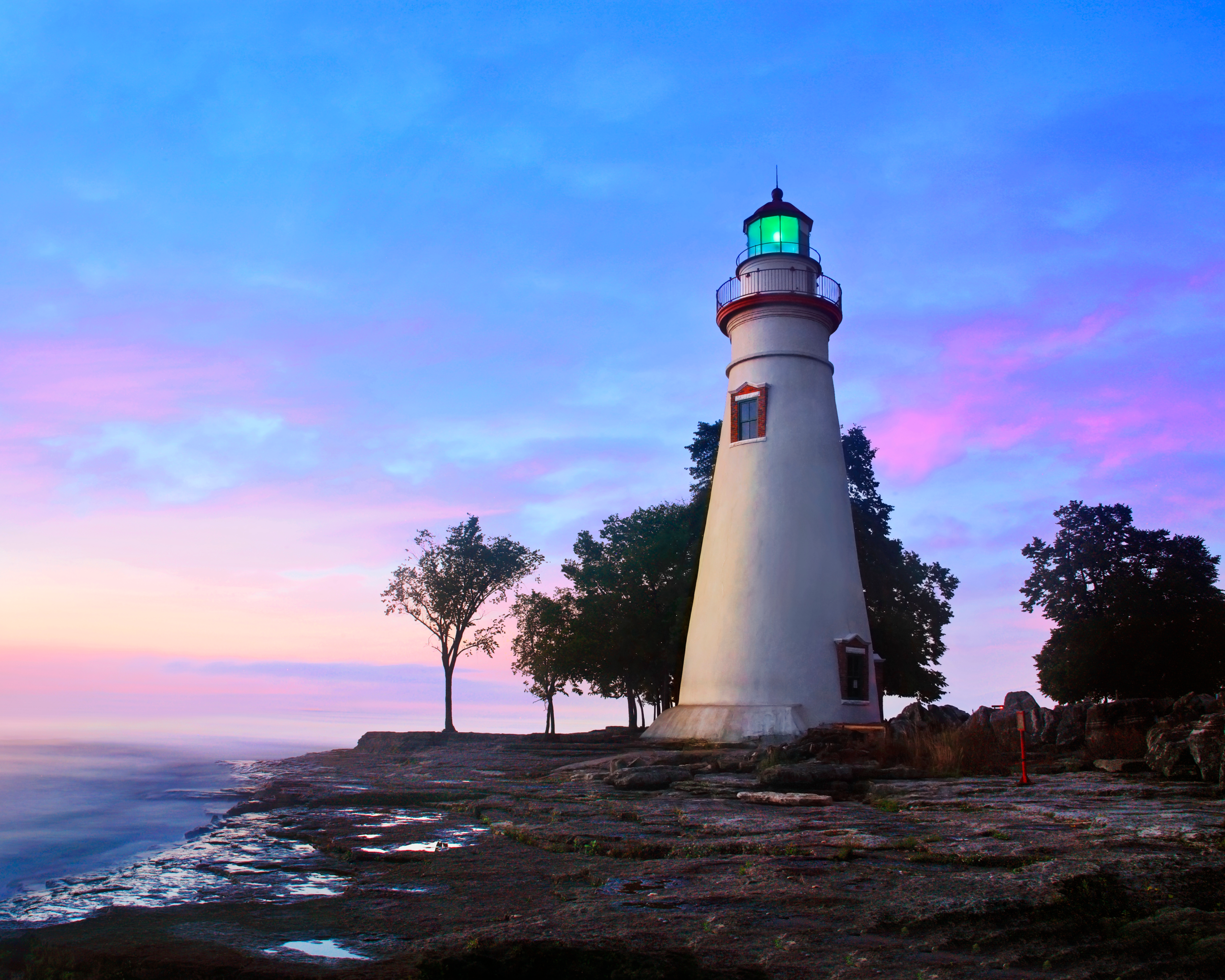 Marblehead Lighthouse glowing at dawn on the rocky Lake Erie shoreline in Marblehead, Ohio.